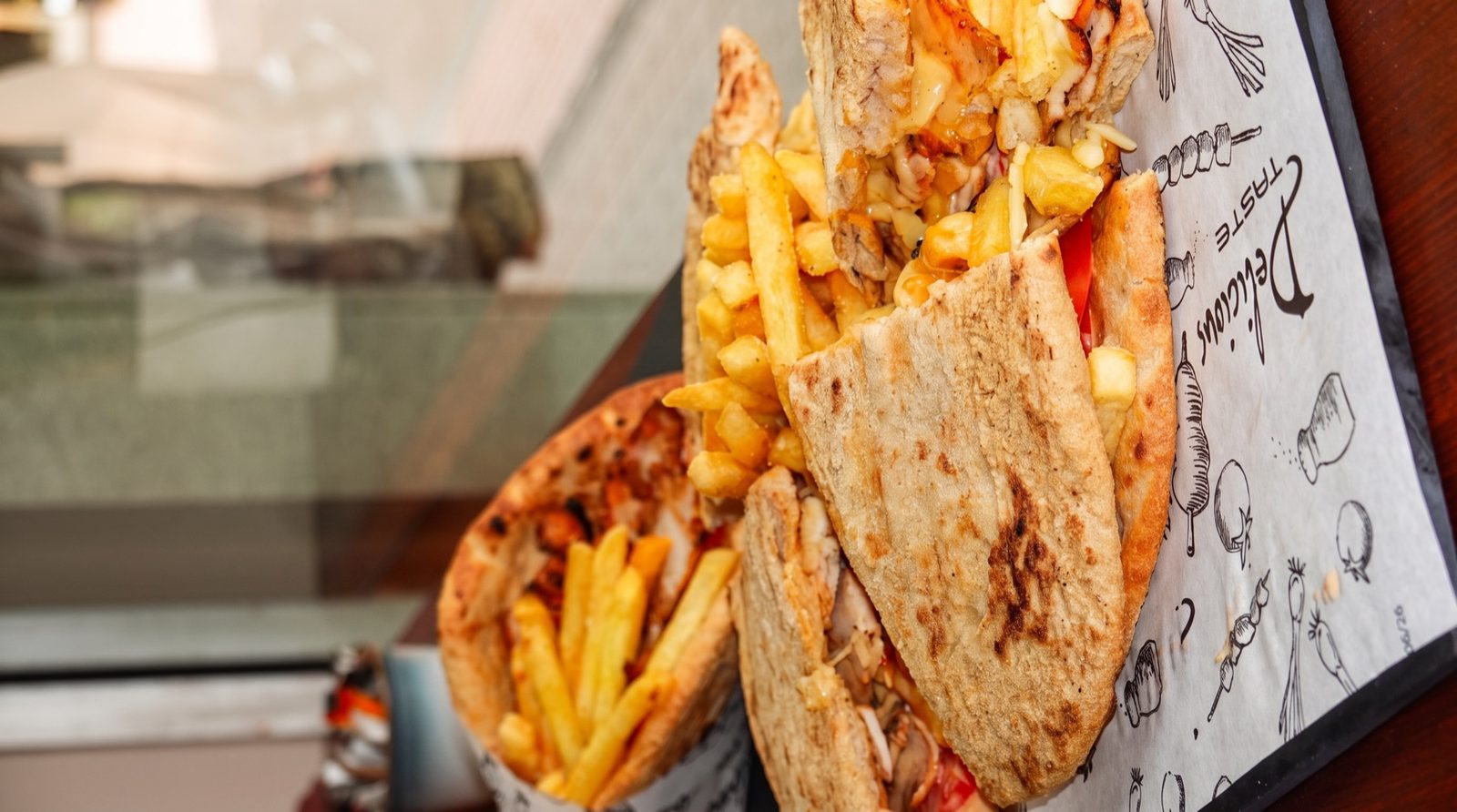 Two loaded Greek pita gyros with chips on branded paper, on our Instagram