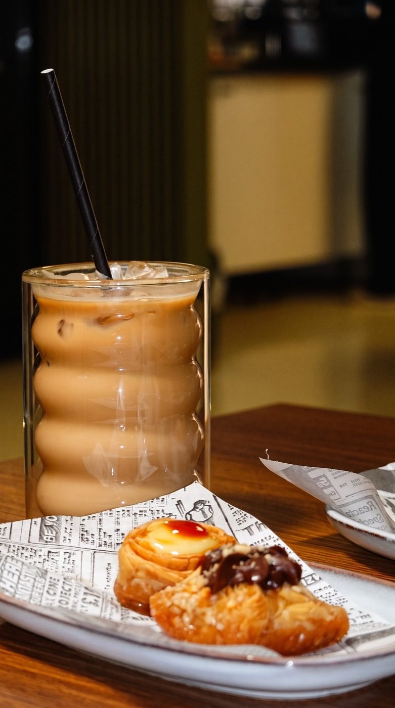 Iced coffee in a ribbed glass beside two pastries, on our Instagram