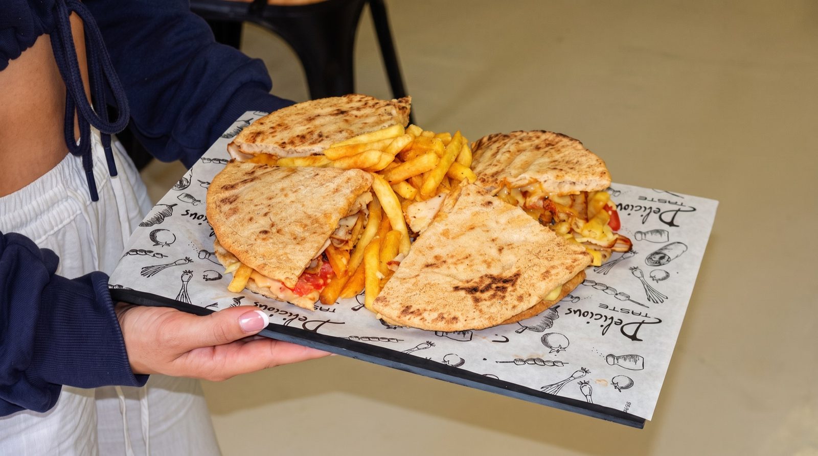 A tray of freshly grilled Greek chicken and chips loaded pitas on branded paper