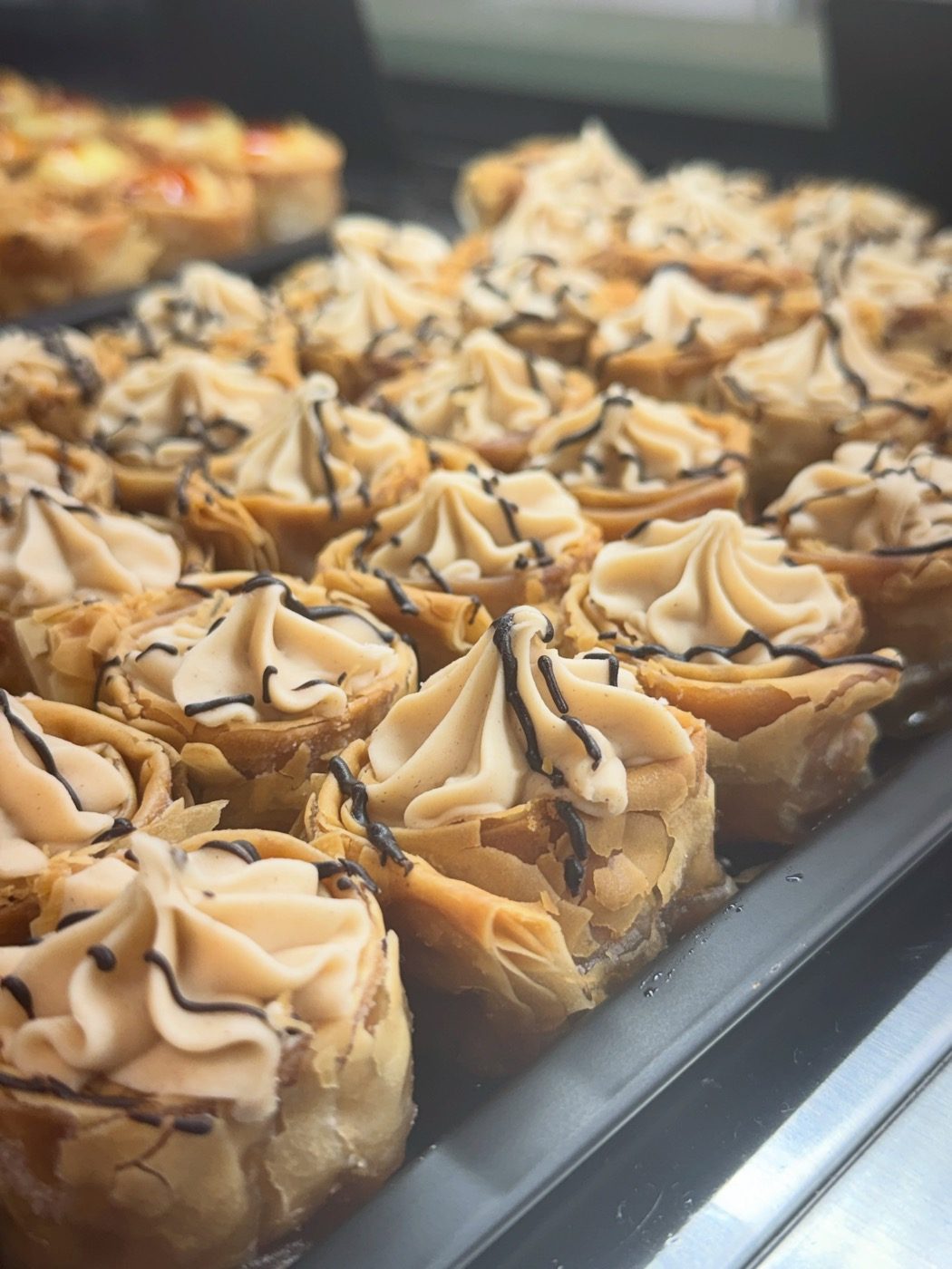 Tray of mini filo baklava cups topped with cream and chocolate in the counter