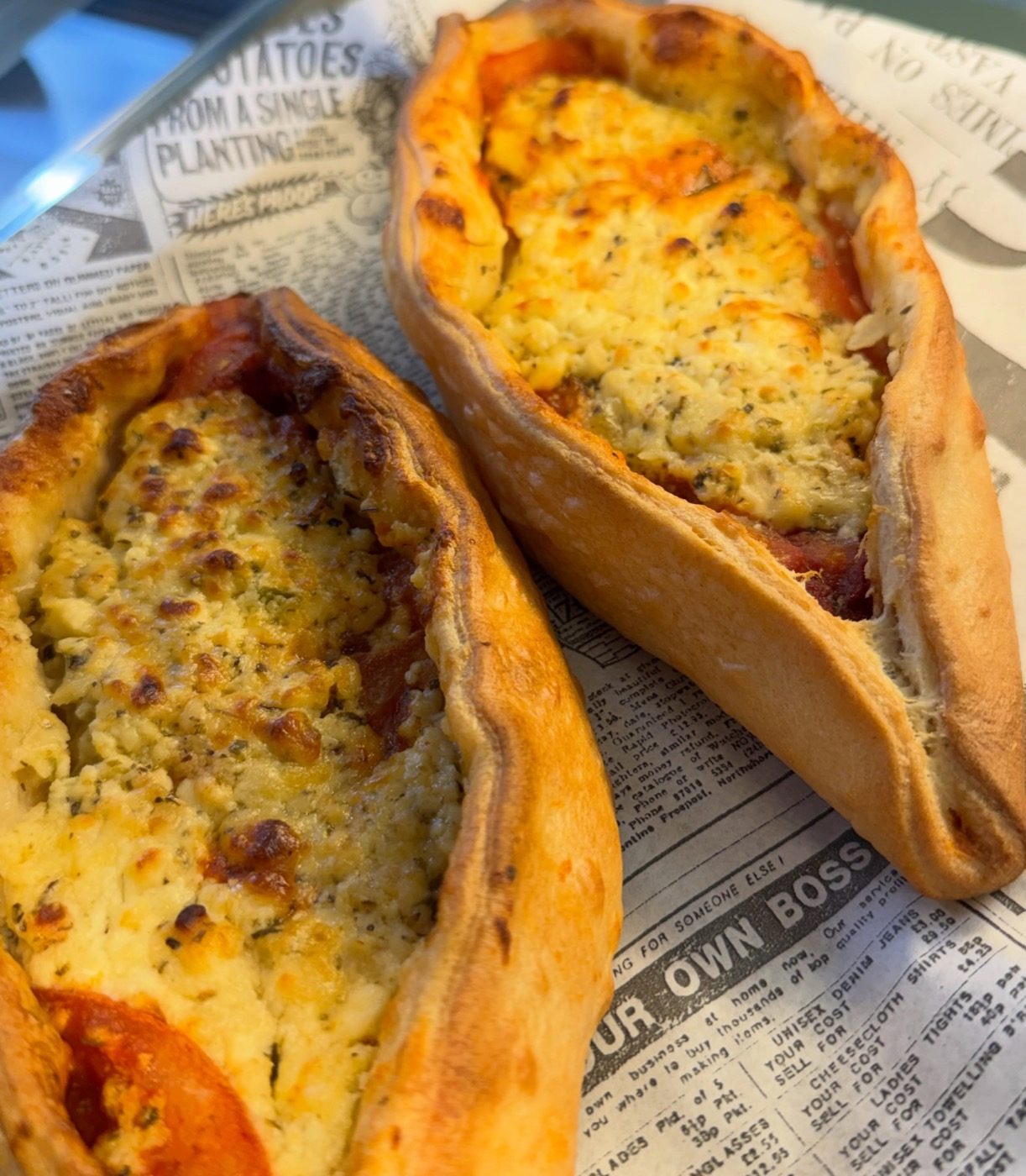 Two freshly baked peinirli cheese boats on newspaper-print paper