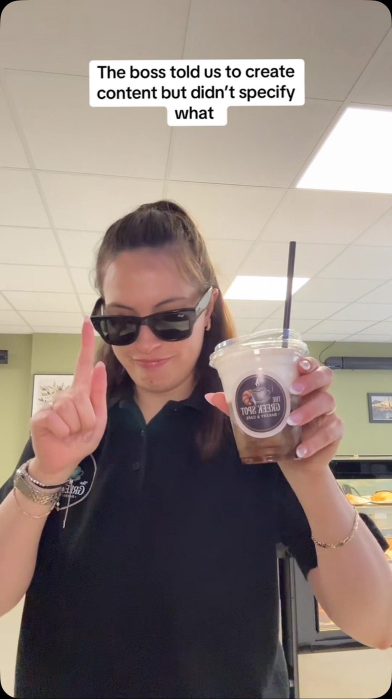 One of the team holding up a Greek Spot iced coffee in the cafe